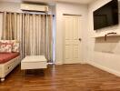 Living room with wooden floor, couch, coffee table, wall-mounted TV, air conditioner, and curtains