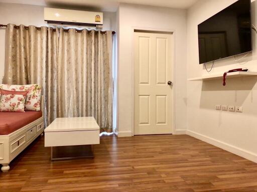 Living room with wooden floor, couch, coffee table, wall-mounted TV, air conditioner, and curtains