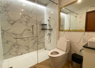 Modern bathroom with marble walls, large mirror, and glass shower enclosure