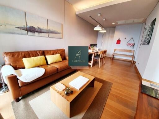 Cozy living room with a brown leather sofa, wooden coffee table, dining area and artwork on the wall