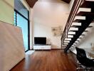 Living room with wooden floor, television, and staircase