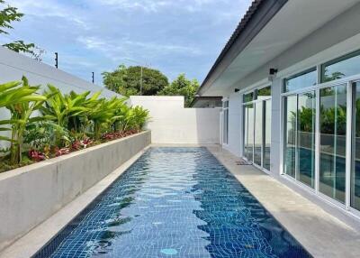 Outdoor swimming pool beside a modern building with glass windows and tropical plants