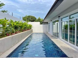 Outdoor swimming pool beside a modern building with glass windows and tropical plants