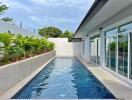 Outdoor swimming pool beside a modern building with glass windows and tropical plants