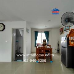 Kitchen and dining area with dining table, refrigerator, wall clock, and window with curtains.