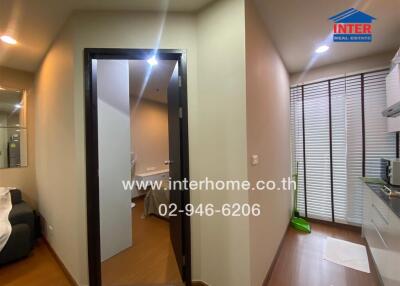 Photo of an apartment interior with visible restroom door, living area, and partial kitchen.