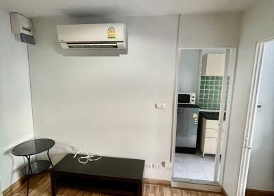 Living room with air conditioning unit, coffee table, and view into the kitchen