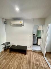 Living room with air conditioning unit, coffee table, and view into the kitchen