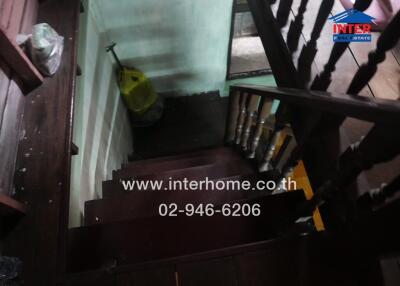 Wooden staircase with dark brown steps and railing, and a cleaning mop in the corner