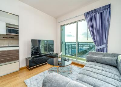 Bright living room with a large window, modern grey sofa, glass coffee table, and a large TV