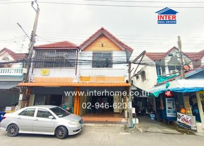 Street view of a two-story building with nearby shops and a parked car