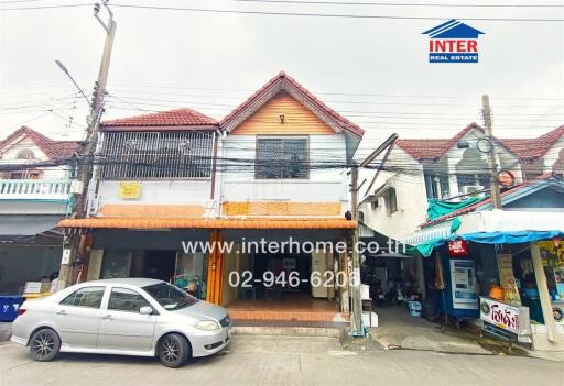 Street view of a two-story building with nearby shops and a parked car