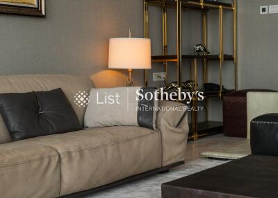 Living room with beige leather sofa and dark cushions, a modern lamp, and a stylish shelving unit.