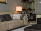 Living room with beige leather sofa and dark cushions, a modern lamp, and a stylish shelving unit.