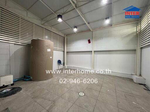 spacious indoor utility or storage room with protective roofing and a large water tank