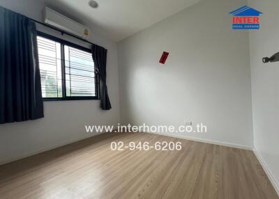 Unfurnished bedroom with wooden flooring and window with curtains