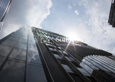 Modern glass exterior of a high-rise building with surrounding buildings and a partly cloudy sky