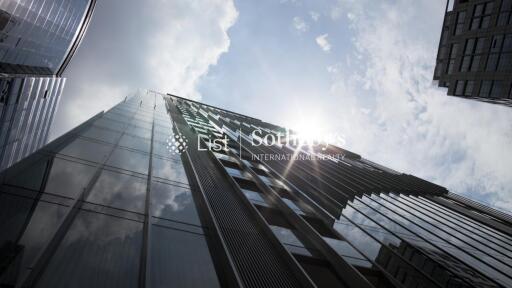 Modern glass exterior of a high-rise building with surrounding buildings and a partly cloudy sky