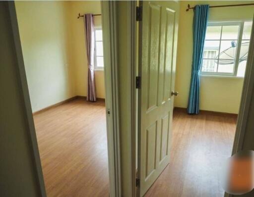 Bedroom with wooden floor and two windows with curtains