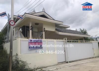 Exterior view of a residential house with a gated entrance and contact information displayed on a banner