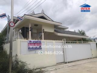 Exterior view of a residential house with a gated entrance and contact information displayed on a banner