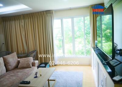 Well-lit living room with large windows, cozy sofa, coffee table, and television