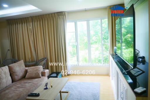 Well-lit living room with large windows, cozy sofa, coffee table, and television