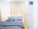 Small bedroom with a gray bedspread, white wardrobe, and beige curtains.