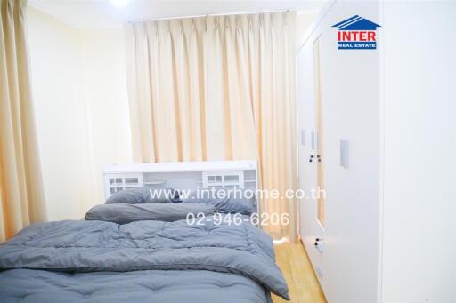 Small bedroom with a gray bedspread, white wardrobe, and beige curtains.