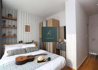 Cozy bedroom with a bed, guitar, hat, and decorative items on a shelf.