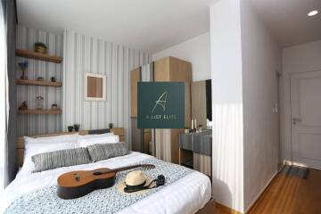 Cozy bedroom with a bed, guitar, hat, and decorative items on a shelf.