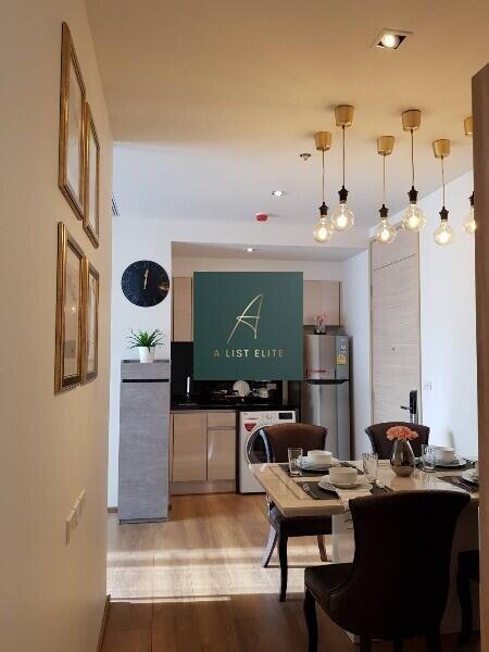 Modern kitchen and dining area with wooden flooring, paintings, and decorative lighting.