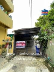 Front view of a property with a carport and surrounding greenery.