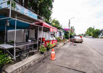 Street side with a food stall, car parked, and greenery