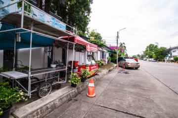 Street side with a food stall, car parked, and greenery