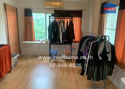 Bedroom with wooden flooring, clothes racks, ironing board, and large window