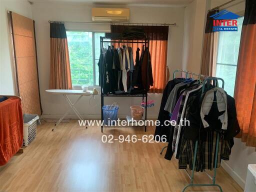 Bedroom with wooden flooring, clothes racks, ironing board, and large window