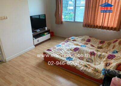 Bedroom with wooden flooring, a television, and a mattress with colorful sheets.