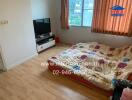 Bedroom with wooden flooring, a television, and a mattress with colorful sheets.