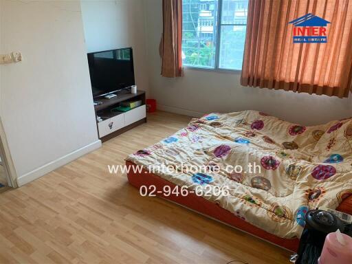 Bedroom with wooden flooring, a television, and a mattress with colorful sheets.