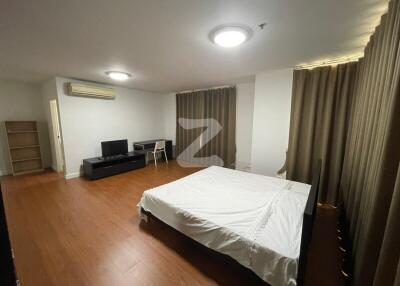 Spacious bedroom with wooden flooring, a large bed, TV stand, and bookshelf