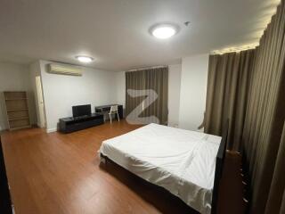 Spacious bedroom with wooden flooring, a large bed, TV stand, and bookshelf