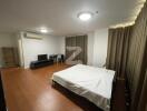 Spacious bedroom with wooden flooring, a large bed, TV stand, and bookshelf