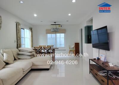 Modern living room with white sectional sofa, flat-screen TV, dining area, and large windows.