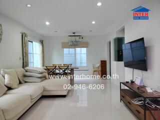 Modern living room with white sectional sofa, flat-screen TV, dining area, and large windows.