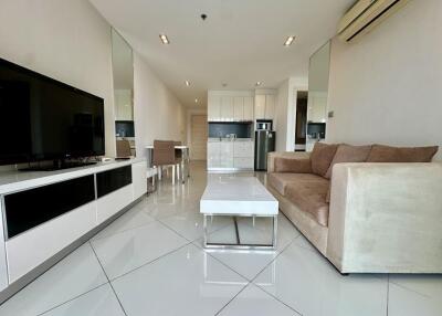 Modern living room with sofa, coffee table, TV, and kitchen in the background