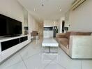 Modern living room with sofa, coffee table, TV, and kitchen in the background