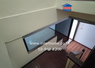 View from the top of a staircase showing a landing area with wooden flooring and a window.