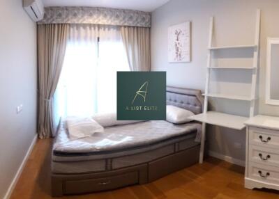 A well-lit bedroom with a large window, a bed, a dressing table, and wall shelves.