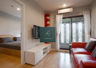 Living area with red sofa and wall-mounted TV adjacent to a bedroom